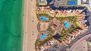 Vista aérea de un resort con múltiples piscinas, una playa y un estacionamiento.