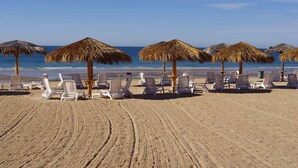 Une plage dotée de parasols en chaume, de chaises longues blanches et offrant une vue dégagée sur l’océan.