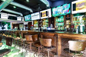 A bar with multiple screens displaying sports content, a variety of liquor bottles, and vintage bar stools.
