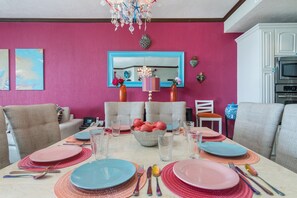 A dining area with a pink wall, a chandelier, and a table set for four with plates, glasses, and cutlery.