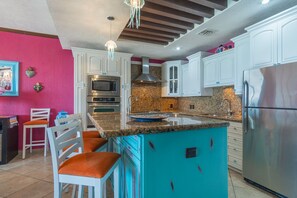 A kitchen with white cabinets, a turquoise island, stainless steel appliances, and orange chairs.