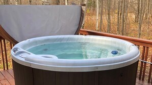 A hot tub on a wooden deck with a bench in front.