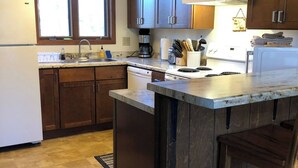 A kitchen with wooden cabinets, a large island, a refrigerator, a sink, and a window.