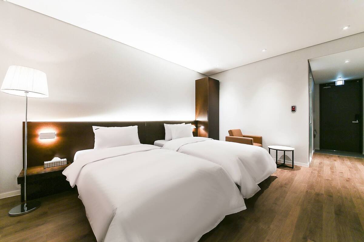 Quarto de hotel moderno com duas camas, uma mesa de cabeceira, um abajur e uma mesinha.