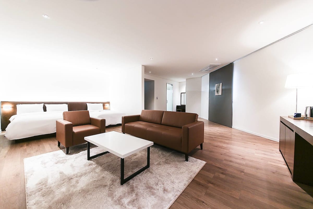 Quarto de hotel moderno com uma cama, dois sofás, uma mesa de centro e uma escrivaninha com abajur.