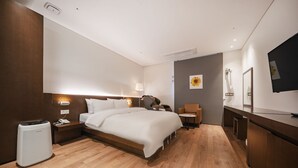 A modern hotel room with a large bed, bedside table, lamp, and a small desk with a chair. - Golden River Hotel (Gwangmyeong)