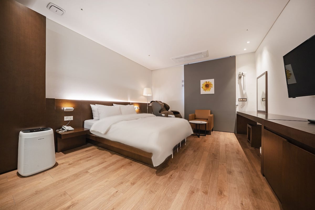 Quarto de hotel moderno com uma cama grande, mesa de cabeceira, luminária e pequena escrivaninha com cadeira.