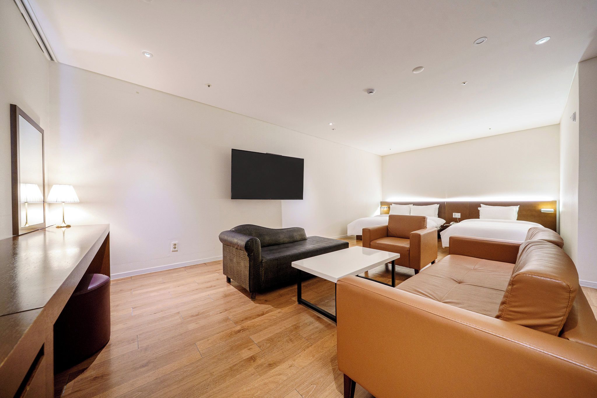 Una habitación de hotel moderna con una televisión de pantalla plana montada en la pared, un sofá, una mesa de centro y un escritorio con lámpara.