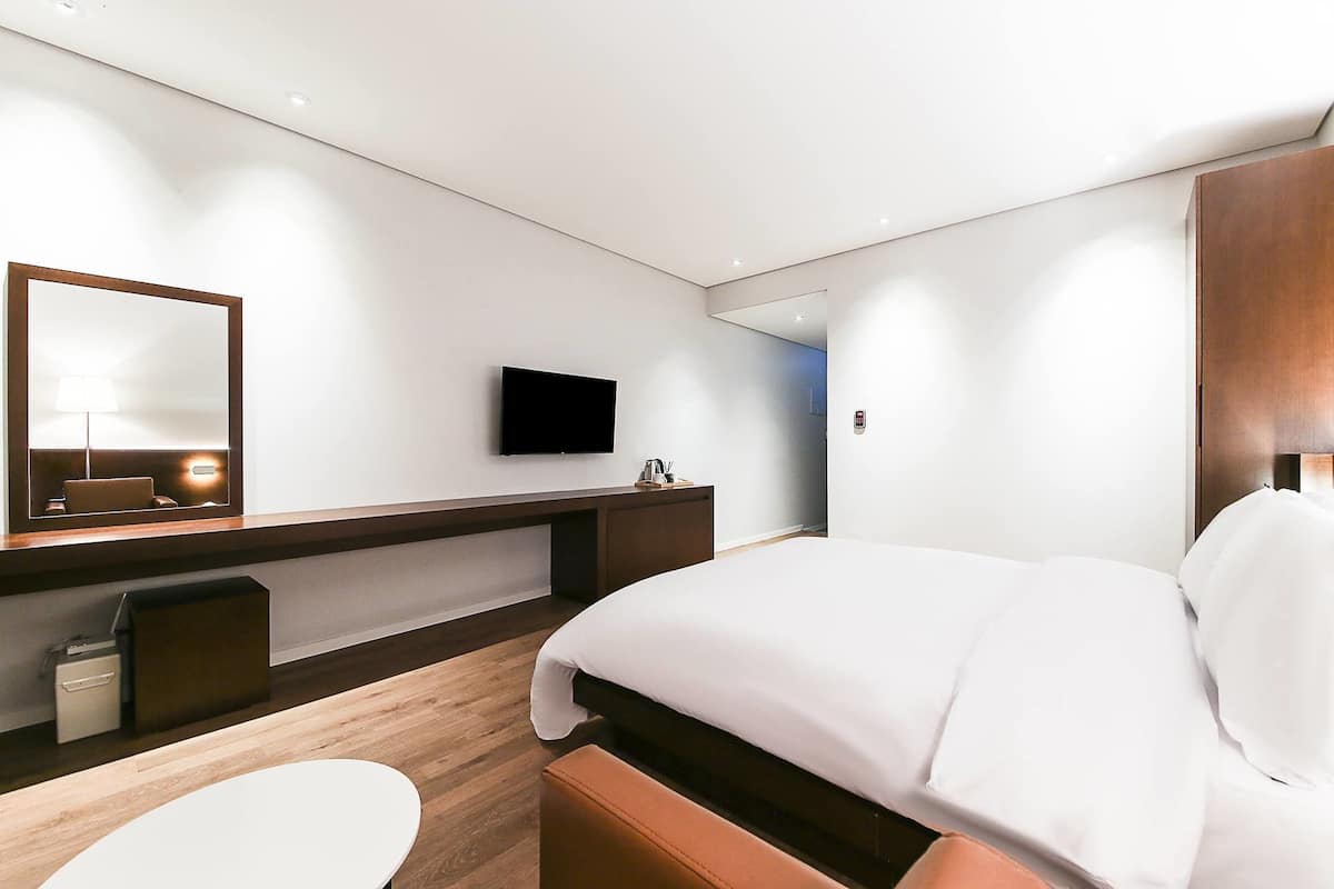 Quarto de hotel moderno com cama, escrivaninha, televisão de tela plana, espelho e mesa de cabeceira.