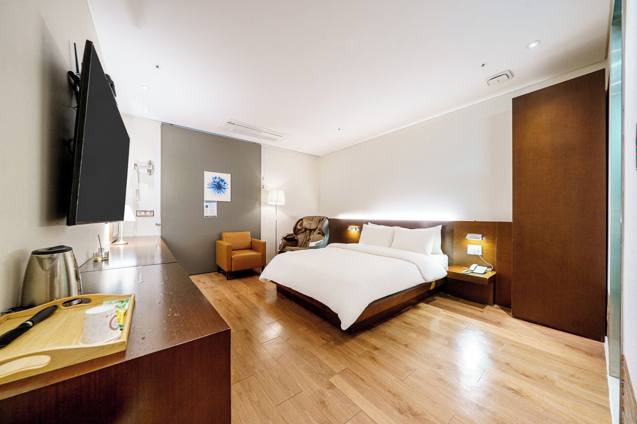 Ein Hotelzimmer mit einem Bett, einem Nachttisch, einem Sessel und einem an der Wand befestigten Fernseher.