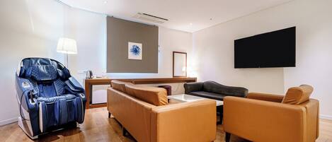 A modern living room with a massage chair, sofas, a coffee table, and a flat-screen TV.