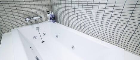 Un baño moderno con una bañera grande, paredes con azulejos y una zona de ducha.