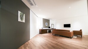 A modern, minimalist living room with a wooden floor, a brown sofa set, a flat-screen TV mounted on the wall, and a large mirror above the sofa. - Golden River Hotel (Gwangmyeong)