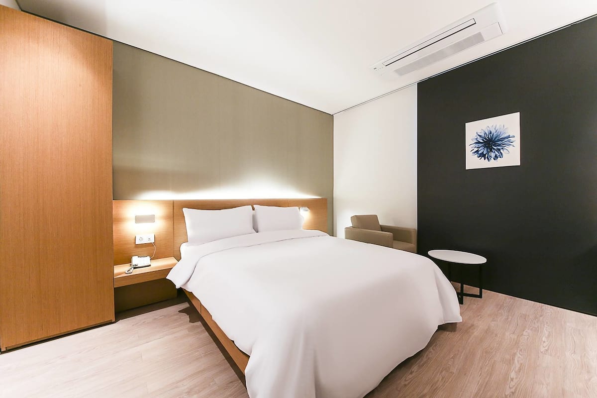 Quarto de hotel moderno com cama, mesa de cabeceira, luminária e uma pequena mesa redonda.
