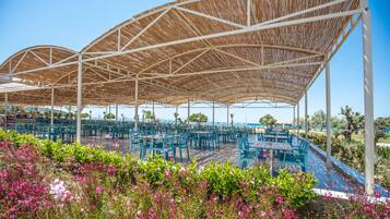 An outdoor dining area with a covered seating arrangement and a poolside view.