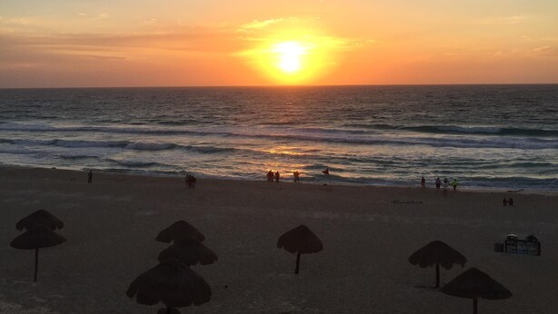 Uma praia com um pôr do sol, guarda-sóis e pessoas.