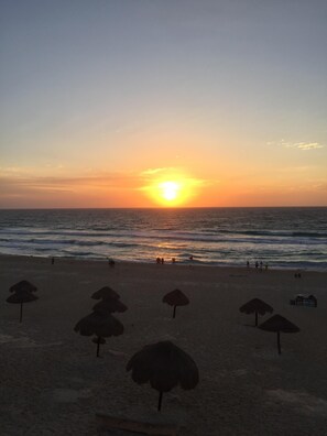 Una playa con un atardecer, sombrillas y gente.