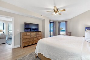 A bedroom with a large bed, wooden dresser, ceiling fan, and a TV. - Refreshing Gulf Breeze and Spectacular views of the Gulf of Mexico! (Orange Beach)