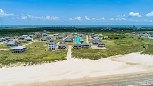 Vista aérea de un complejo turístico costero con varias villas frente a la playa, un paseo central y una playa de arena.