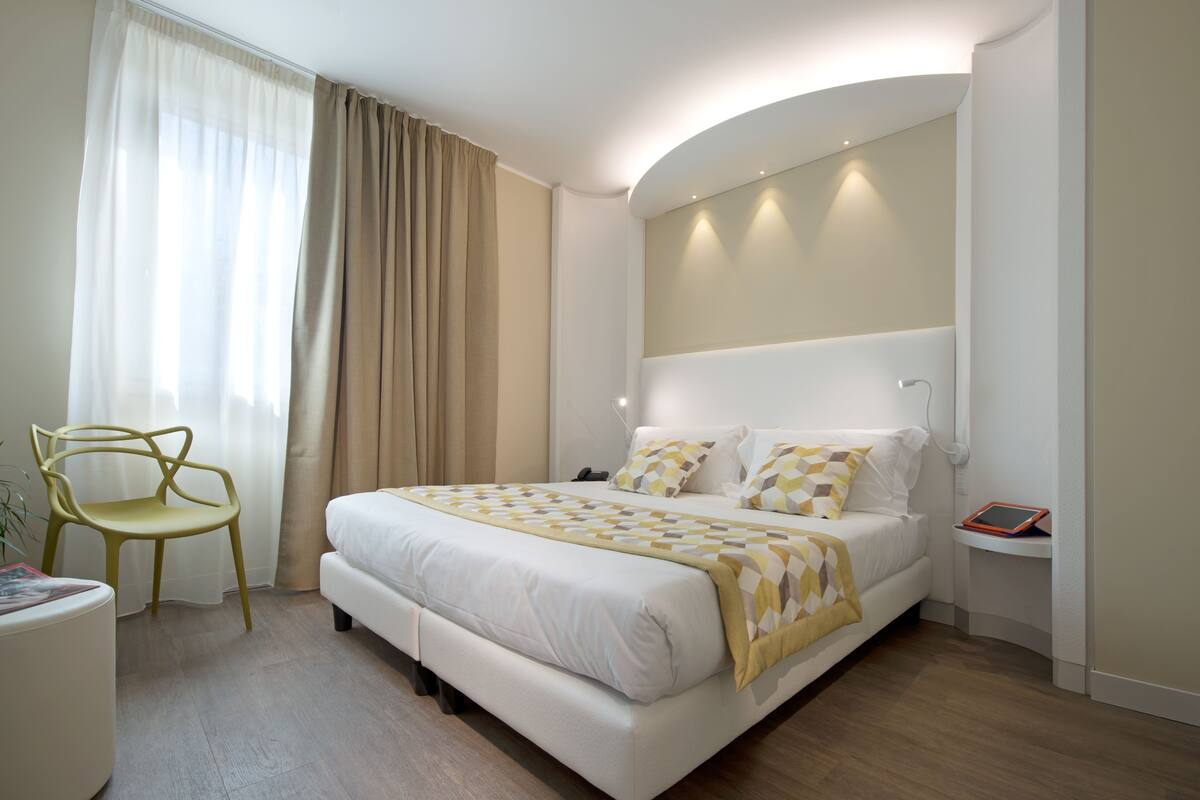A modern hotel room with a large bed, a bedside table, a chair, and a bedside lamp.