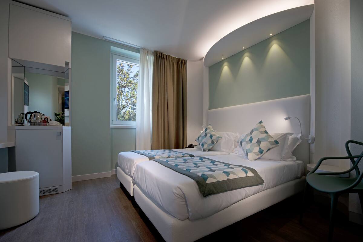 A modern bedroom with a large bed, a bedside table, a chair, and a window with curtains.