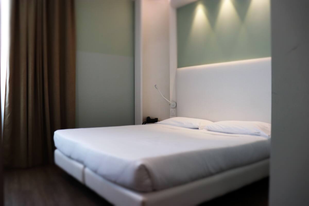 A neatly made bed in a hotel room with a white headboard, a bedside table, and a lamp.