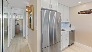 Una cocina moderna con armarios blancos, un refrigerador de acero inoxidable y un salpicadero con el letrero 'ALOHA'.