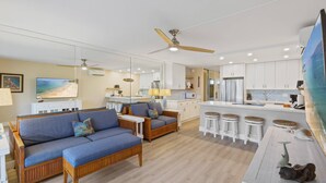 Una sala moderna con un sofá, una zona de comedor con taburetes y una cocina con armarios blancos.