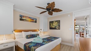 Una habitación de hotel con una cama de madera, mesitas de noche blancas, un ventilador de techo y obras de arte en las paredes.