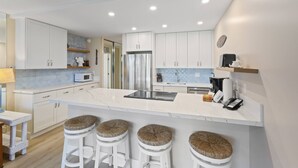 Una cocina moderna con armarios blancos, una isla central con taburetes y microondas integrado.
