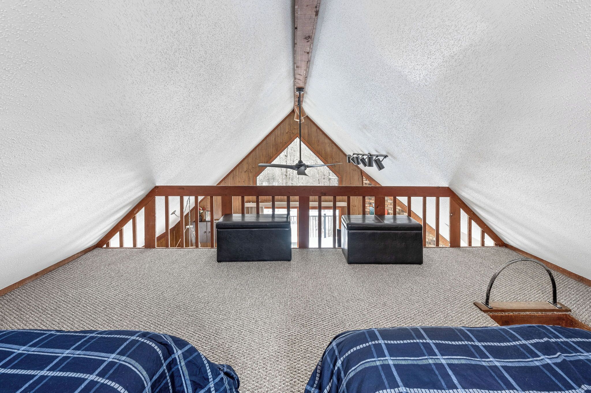 A cozy, triangular tent-like room with a wooden ceiling and two black ottomans.