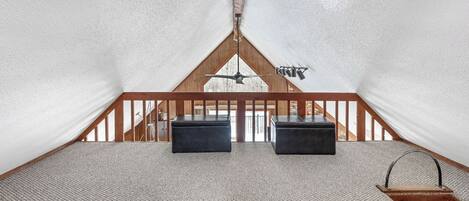 A cozy, triangular tent-like room with a wooden ceiling and two black ottomans.