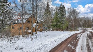 A rustic building with a snow-covered landscape, a dirt road, and a clear sky. - A Cozy Vacation Home with a Sauna & Beautiful Nature View (Ironwood)