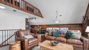 A spacious living area with leather sofas, a wooden coffee table, and a rustic barrel. A kitchen is visible in the background with a dining table and chairs. - A Cozy Vacation Home with a Sauna & Beautiful Nature View (Ironwood)