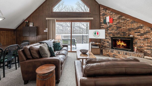 A loft-style living room with a fireplace, leather sofas, and a large window overlooking a snowy deck. - A Cozy Vacation Home with a Sauna & Beautiful Nature View (Ironwood)
