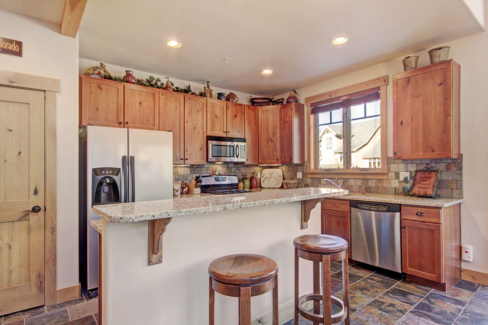A kitchen with wooden cabinets, a granite countertop, a refrigerator, a microwave, a stove, and a dishwasher.
