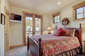 Una camera da letto con un letto in legno, una TV a parete e vista all'esterno attraverso ampie finestre.