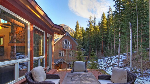 A cozy patio with wicker furniture and a stone table, overlooking a forested area with a mountain in the background. - Magnificent Townhome/Private Garage/Pool & Hot Tub Access/On the Shuttle Route! (Keystone)