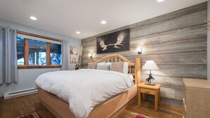 A bedroom with a wooden bed, a nightstand with a lamp, a wooden headboard, and a window with curtains. - JHRL - Nez Perce D2, Recently updated 3-bedroom Mountain Decor - 1 mile from Grand Teton NP (Teton Village)