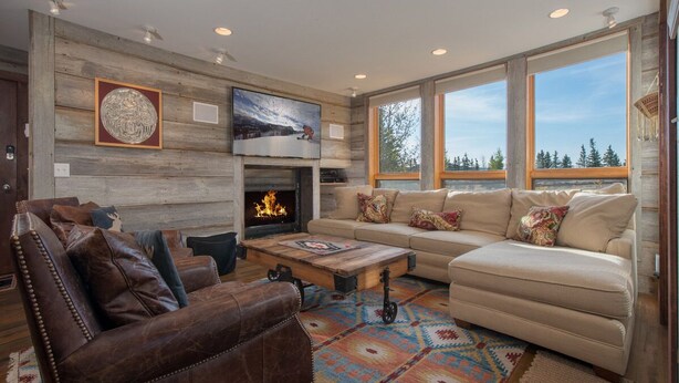A cozy living room with a fireplace, leather sofas, and a large window offering a view of trees. - JHRL - Nez Perce D2, Recently updated 3-bedroom Mountain Decor - 1 mile from Grand Teton NP (Teton Village)