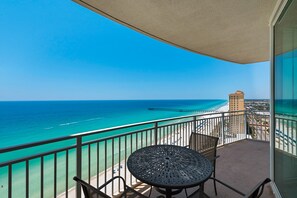Balcón con mesa y sillas, con vista a una playa y al océano.