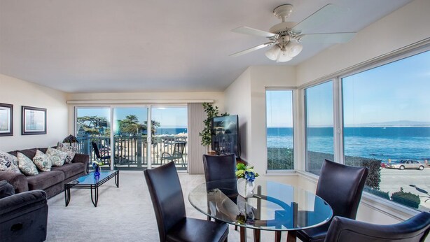 Een ruime woonkamer met balkon en uitzicht op zee, ingericht met een bank, fauteuils en een salontafel.