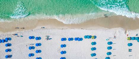 Vue aérienne d’une plage où des parasols bleus sont disposés en forme de cœur.