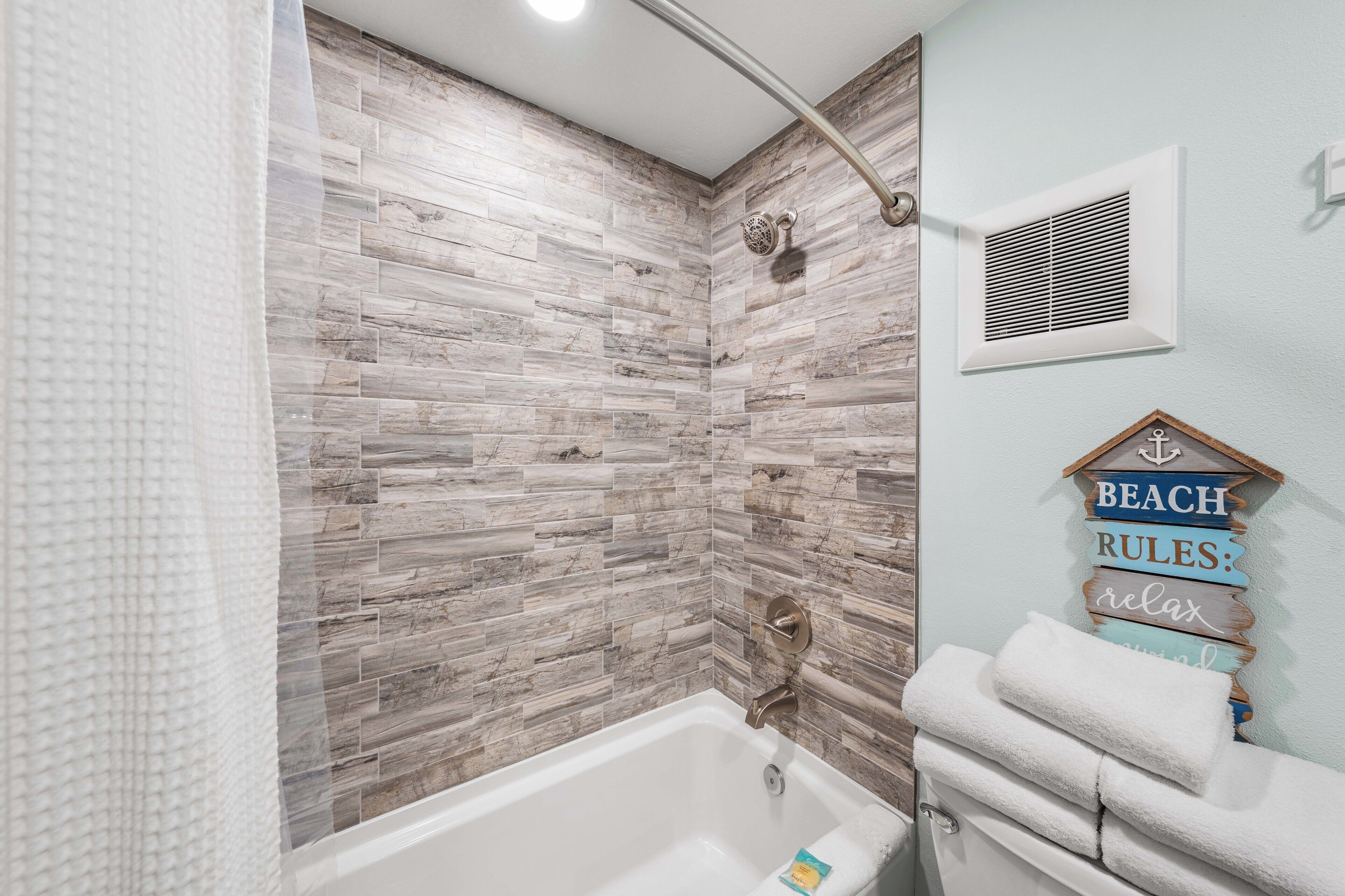 A bathroom with a wooden-textured wall, a shower, and a towel rack with a sign.
