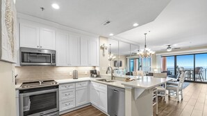 A modern kitchen with white cabinetry, stainless steel appliances, and a large island with seating. - 1603W - Stunning 2BR Beachfront Condo! (Orange Beach)