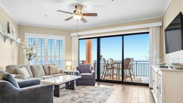 A spacious living room with a ceiling fan, a large window, and a balcony with a view. - 1603W - Stunning 2BR Beachfront Condo! (Orange Beach)