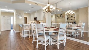 A spacious dining area with a large round table, white chairs, and a chandelier. - 1603W - Stunning 2BR Beachfront Condo! (Orange Beach)