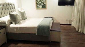 Una cama bien tendida con un edredón gris, una mesita de noche con una lámpara y un cuadro en la pared.