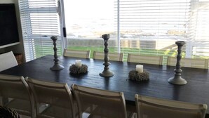 A dining table with four candle holders and candles, surrounded by chairs, in a room with large windows. - Waterfront Apartment C3 (Swakopmund)