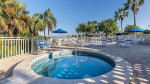 A circular pool with lounge chairs and umbrellas, surrounded by palm trees and a white fence. - Salt Life Cottage U420 - Little Harbor Beach Resort Tampa Bay (Ruskin)